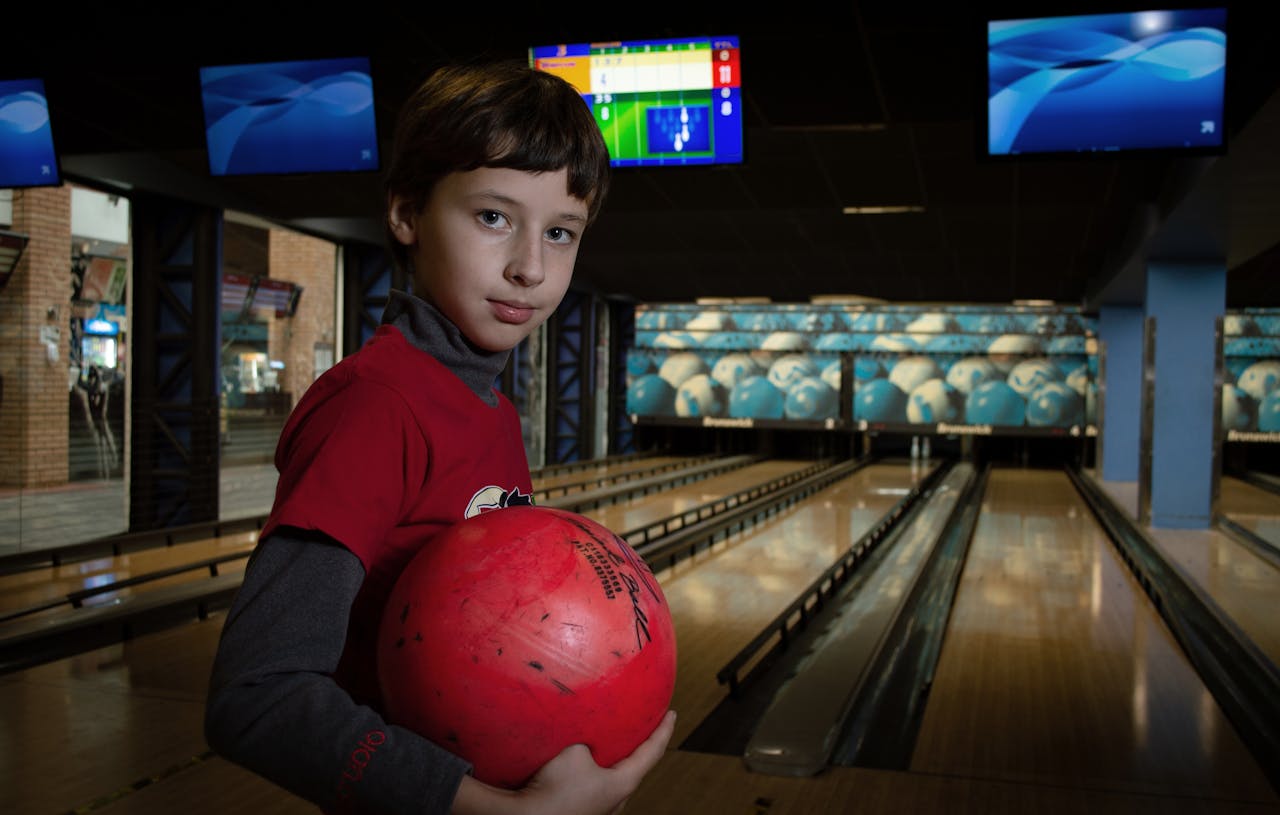 A young boy smiles while holding a bowling ball at a bowling alley indoors.